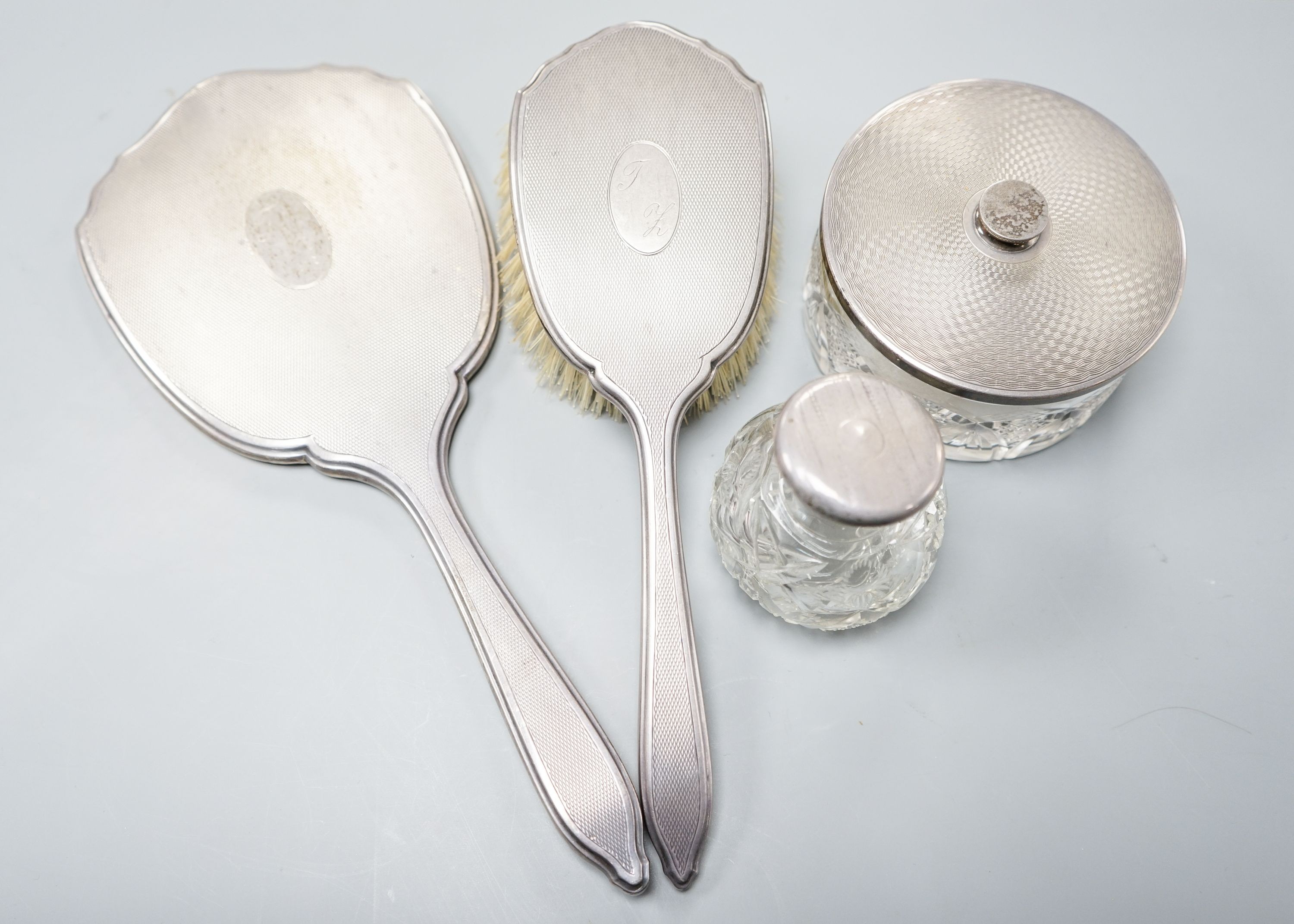 A silver-backed hand mirror and hairbrush, a silver-mounted scent bottle and a powder bowl.